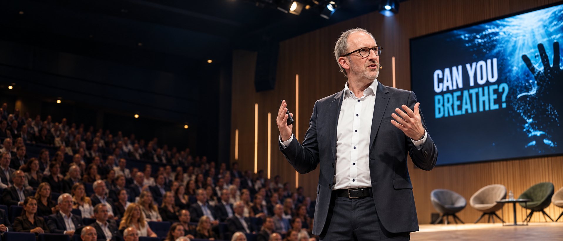 Joachim De Vos speaking on stage to a full auditorium.