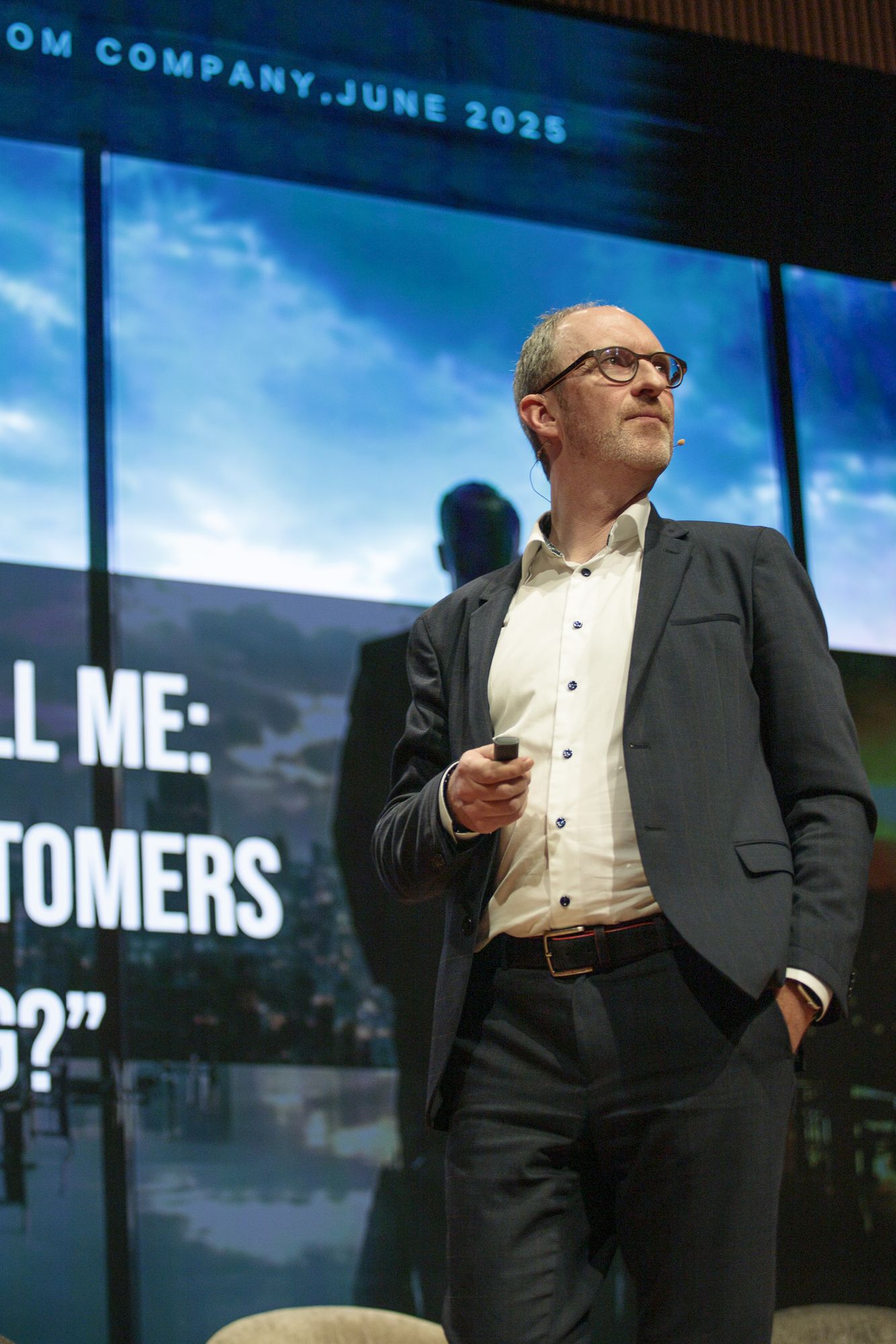 Joachim De Vos speaking on stage, clicker in hand, looking toward the audience.